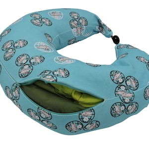 Op de afbeelding: Een turquoise reisnekkussen met een ritsvak en een zwart-witte wereldkaartpatroon. Het kussen is gevuld met groene en gele stof.