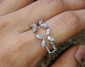 Puede incluir: Un anillo de plata con un delicado diseño de hojas y pequeñas piedras brillantes. El anillo está abierto en la parte posterior y tiene un estilo único y moderno.
