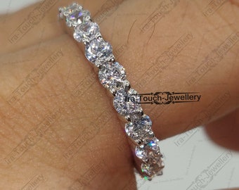 May include: A silver eternity band with a row of round, clear cubic zirconia stones.