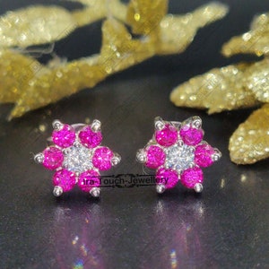 May include: A pair of silver earrings with a flower design. Each earring features a cluster of pink gemstones surrounding a single, larger, clear gemstone in the centre.