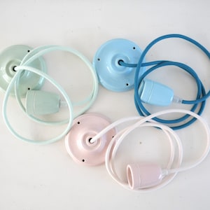 Puede incluir: Vista aérea de cuatro lámparas colgantes de cerámica en colores pastel: verde menta, azul claro, rosa y blanco. Cada lámpara incluye una placa de techo, cable y portalámparas a juego. Los cables están envueltos en tela.