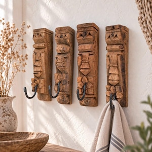 Può includere: Quattro ganci appendiabiti verticali da parete realizzati in legno marrone invecchiato con intricati motivi geometrici e floreali intagliati a mano. Ogni pezzo presenta un gancio in metallo nero curvo alla base, uno sostiene un asciugamano beige.