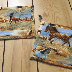 May include: Two brown and blue quilted pot holders with a horse design and a wooden button. The pot holders are on a wooden surface.