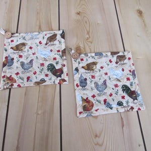 May include: Two square pot holders with a beige background and a repeating pattern of chickens and red flowers. Each pot holder has a wooden button and a fabric loop. The pot holders are made of fabric.