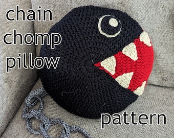 Puede incluir: Un cojín Chain Chomp negro tejido a ganchillo con boca roja y beige, un ojo beige y una cadena gris. El texto "chain chomp pillow pattern" se muestra en la imagen.