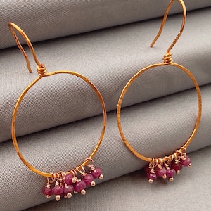 May include: Gold hoop earrings with a hammered finish and dangling pink gemstone beads.