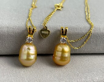 May include: Two gold necklaces with a golden pearl pendant and a small clear stone. Each pendant has a small clear stone on the top. The necklaces are on a light brown fabric background. The tag on the necklace reads "S925".