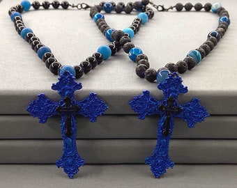 Può includere: Due collane con perline di agata blu e roccia lavica nera. Ogni collana ha un ciondolo a forma di croce ornata blu e nera.
