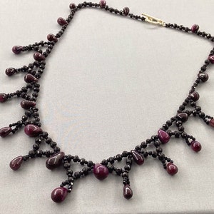 Peut inclure: Un collier noir et bordeaux avec un design en forme de goutte. Le collier est composé de petites perles noires et de plus grosses perles bordeaux.