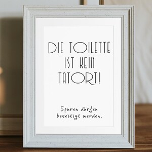 May include: A framed print with the text "DIE TOILETTE IST KEIN TATORT!" in black, with the text "Spuren d&uuml;rfen beseitigt werden." below. The frame is a light gray color and the background is white.