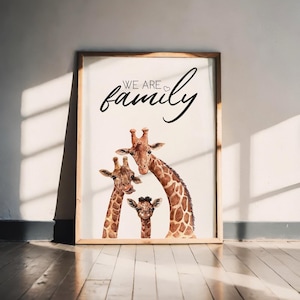 May include: A framed art print showing a giraffe family. The giraffes are illustrated in watercolour with brown and tan markings. The text "WE ARE family" is written in a cursive font above the giraffes.