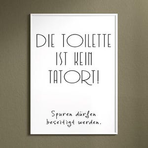 May include: A framed white print with black text that reads "DIE TOILETTE IST KEIN TATORT!" and "Spuren d&uuml;rfen beseitigt werden." The print is displayed on a neutral-colored wall.