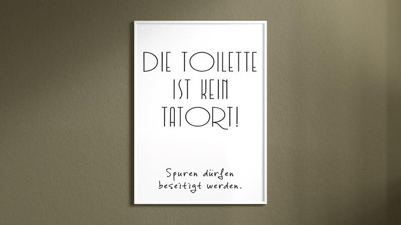 May include: A framed white print with black text that reads "DIE TOILETTE IST KEIN TATORT!" and "Spuren d&uuml;rfen beseitigt werden." The print is displayed on a neutral-colored wall.