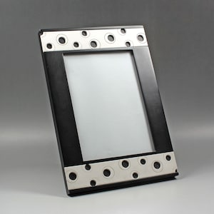 Puede incluir: Marco de fotos negro con un borde blanco que presenta un patrón repetido de círculos. El marco está hecho de madera y tiene un acabado mate.