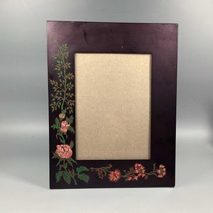 Puede incluir: Un marco de fotos de color morado oscuro con un diseño floral pintado en el borde. Las flores son rosas y verdes.