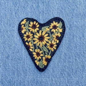 Puede incluir: Parche bordado en forma de corazón con diseño de girasoles. El parche tiene un fondo azul oscuro con girasoles amarillos y marrones y hojas verdes. Para ropa o accesorios.