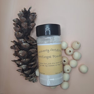 May include: A small glass jar with a black lid containing a white powder. The jar has a yellow label that reads "Heavenly Antidote Antifungal Powder" and lists uses for the powder, such as athlete's foot, jock itch, and moist areas.