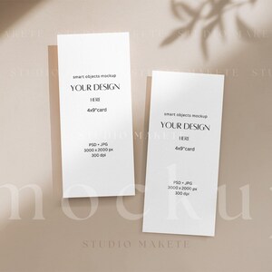 May include: Two white 4x9 inch cards with the text "smart objects mockup" and "YOUR DESIGN HERE" on a beige background. The cards are positioned vertically and are partially in the shadow of a plant.