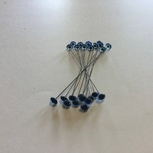 May include: A group of blue and black glass eyes on wire stems. The eyes are arranged in a loose pile.