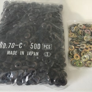 May include: Two bags of black plastic buttons. The bag on the left contains 500 black plastic buttons and has the text "NO.70-C 500 PCS MADE IN JAPAN" printed on it. The bag on the right contains a variety of metal washers.