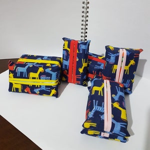 May include: Five blue and yellow fabric tissue boxes with a zebra and giraffe print. The boxes have a red, pink, or yellow trim.
