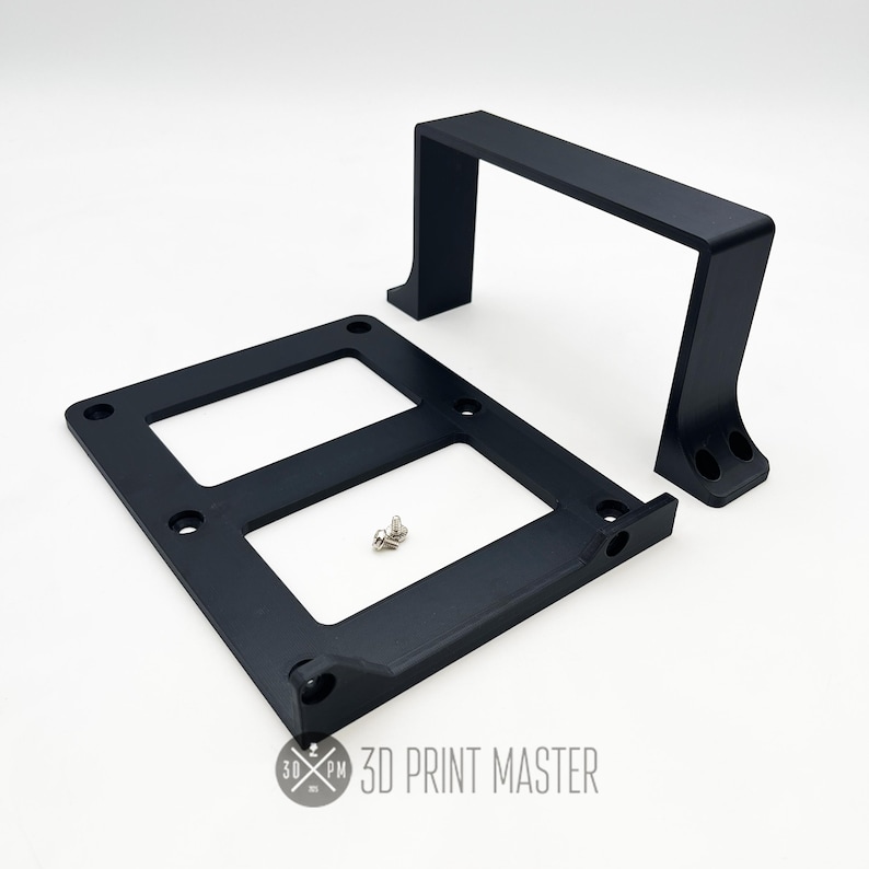 May include: Black 3D printed plastic bracket with two slots and a handle. The bracket is designed to hold a device or object. 3D Print Master is printed on the bracket.