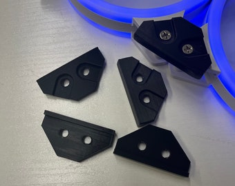 May include: Five black plastic corner brackets with holes for screws. The brackets are designed to be used for mounting a fan or other device to a surface.