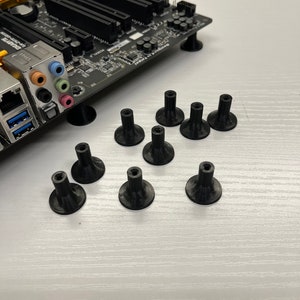 Op de afbeelding: Een close-up van tien zwarte plastic afstandhouders voor een moederbord. De afstandhouders zijn ontworpen om het moederbord boven de behuizing te tillen, waardoor er ruimte is voor componenten.