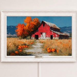 May include: A rectangular digital display framed in white, showing a landscape painting of a red barn in a pumpkin patch with orange trees and mountains under a blue sky. The word SAMSUNG is printed on a small silver plaque at the bottom center.