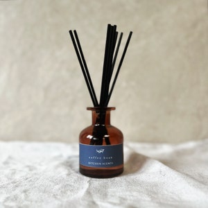 Könnte beinhalten: Ein brauner Glasdiffusor mit schwarzen Schilfrohren und einem blauen Etikett mit der Aufschrift "coffee bean KITCHEN SCENTS".