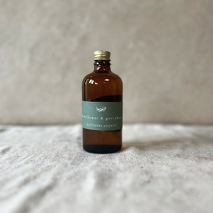 Può includere: Una bottiglia di vetro marrone con un tappo dorato e un'etichetta verde su cui è scritto "elderflower & gooseberry KITCHEN SCENTS".