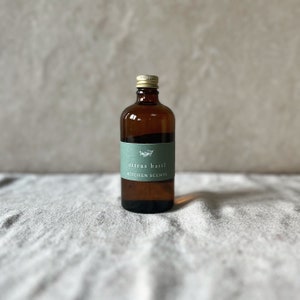 May include: A brown glass bottle with a gold lid and a green label that says "citrus basil KITCHEN SCENTS".