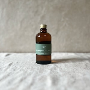 May include: A brown glass bottle with a gold lid and a green label that reads "pomegranate noir kitchen scents".