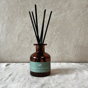 Op de afbeelding: Een bruine glazen diffuser met zwarte rietjes en een groen label met de tekst "bergamot & patchouli KITCHEN SCENTS".