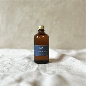 May include: A brown glass bottle with a gold lid and a blue label that reads "olive oil & thyme" and "kitchen scents".