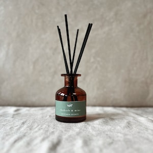 Può includere: Un diffusore di bottiglia di vetro marrone con canne nere e un'etichetta verde che recita "rabarbaro e menta" e "profumi da cucina".