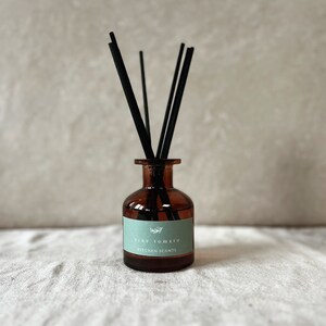 May include: A brown glass bottle with black diffuser sticks and a label that reads "vine tomato kitchen scents".