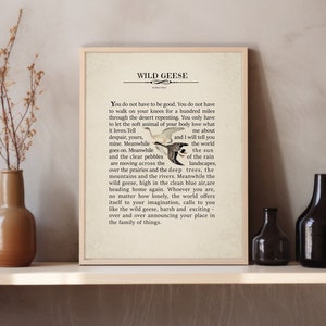 Op de afbeelding: Een ingelijste kunstdruk met het gedicht Wild Geese van Mary Oliver. De tekst is in het zwart gedrukt op een lichtbeige achtergrond, vergezeld van een kleine illustratie van twee vliegende ganzen. De lijst is van lichtgekleurd hout.