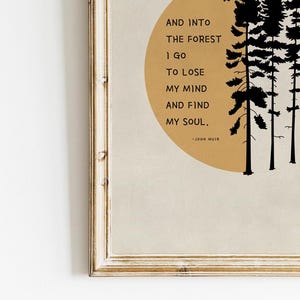 K&ouml;nnte beinhalten: Ein gerahmter Druck mit einem Zitat von John Muir &uuml;ber das Finden seiner Seele im Wald. Das Zitat ist auf einem beigefarbenen Hintergrund mit einer Silhouette von B&auml;umen und einer Sonne gedruckt.