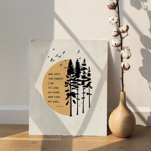 K&ouml;nnte beinhalten: Ein beiger Poster mit einer schwarzen Silhouette eines Waldes mit einem gelben Kreis dahinter. Der Text auf dem Poster lautet "AND INTO THE FOREST I GO TO LOSE MY MIND AND FIND MY SOUL." - JOHN MUIR