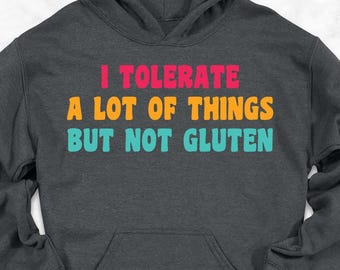 May include: Dark gray hoodie with the text "I TOLERATE A LOT OF THINGS BUT NOT GLUTEN" in colorful letters. The hoodie has a front pocket and a hood. The image also includes jeans, shoes, and a backpack.