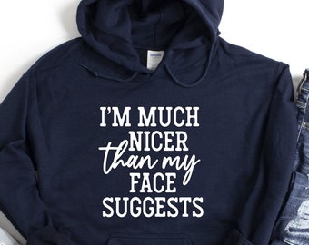 Peut inclure: Un sweat à capuche bleu marine avec le texte "I'm much nicer than my face suggests" imprimé en blanc sur le devant.