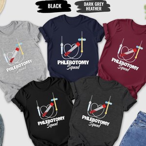 May include: A collection of t-shirts in various colors, including gray, navy, maroon, and black. Each shirt features a graphic of a blood collection tube and the words "Phlebotomy Squad". The shirts are displayed with jeans, shoes, and accessories.