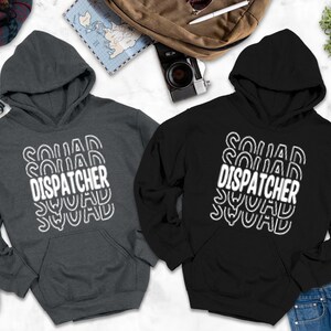 May include: Two hooded sweatshirts, one charcoal gray and one black, with the text "SQUAD DISPATCHER SQUAD" in white. The sweatshirts have a front pocket and a drawstring hood. The image includes accessories like shoes, a backpack, and sunglasses.