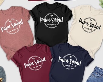May include: A collection of short-sleeved t-shirts in various colors, including heather mauve, black, maroon, navy, and natural. Each shirt features a circular graphic with the text "Papa Squad" and related words. The shirts are displayed with jeans, shoes, and accessories.