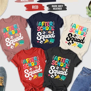 May include: A collection of colorful t-shirts with the text "After School Squad" in a playful font. The shirts are in various colors, including heather mauve, navy, red, dark grey heather, and natural. The design includes school-themed graphics.