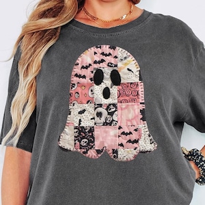 May include: Dark grey t-shirt featuring a patchwork ghost design in pink, black, and white. The ghost has a scalloped edge and is centered on the shirt. The word "PEPPER" is in a white rectangle in the lower right corner.