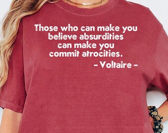 May include: Crimson-colored t-shirt with the quote "Those who can make you believe absurdities can make you commit atrocities. - Voltaire -" printed in white. The shirt is a short-sleeved, crew neck style.