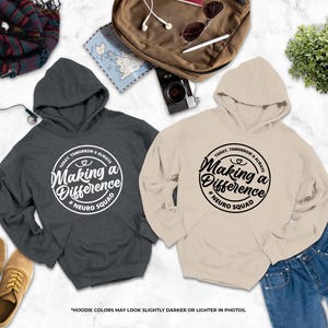 two hooded sweatshirts with the same design, laid out on a marble surface alongside other items such as a camera, a plant, and a pair of shoes.
