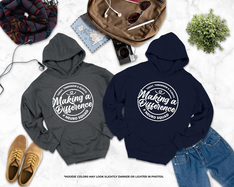 a pair of gray and navy blue hooded sweatshirts with white text, laid out on a marble surface alongside other items such as a backpack, a pair of shoes, and a plant.